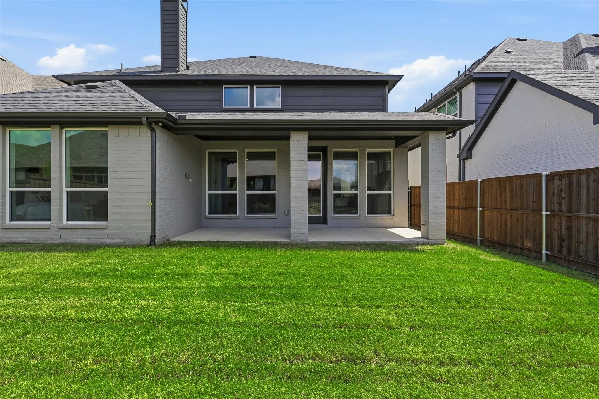 Expansive lawn area featuring a covered patio, brick and siding exterior, multiple windows, and a privacy fence