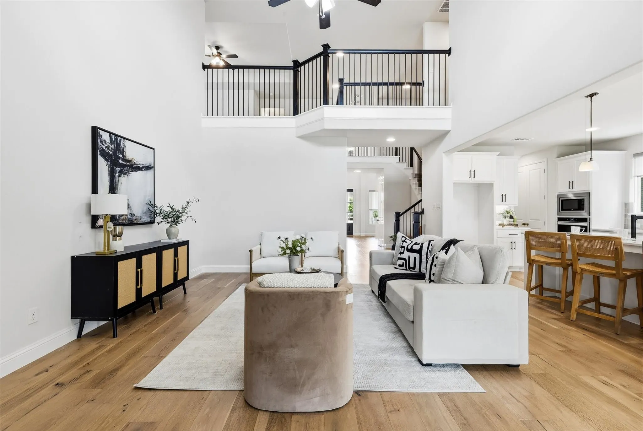 Spacious living area featuring wood-finish flooring, high ceilings, and a second-story overlook with black metal balusters