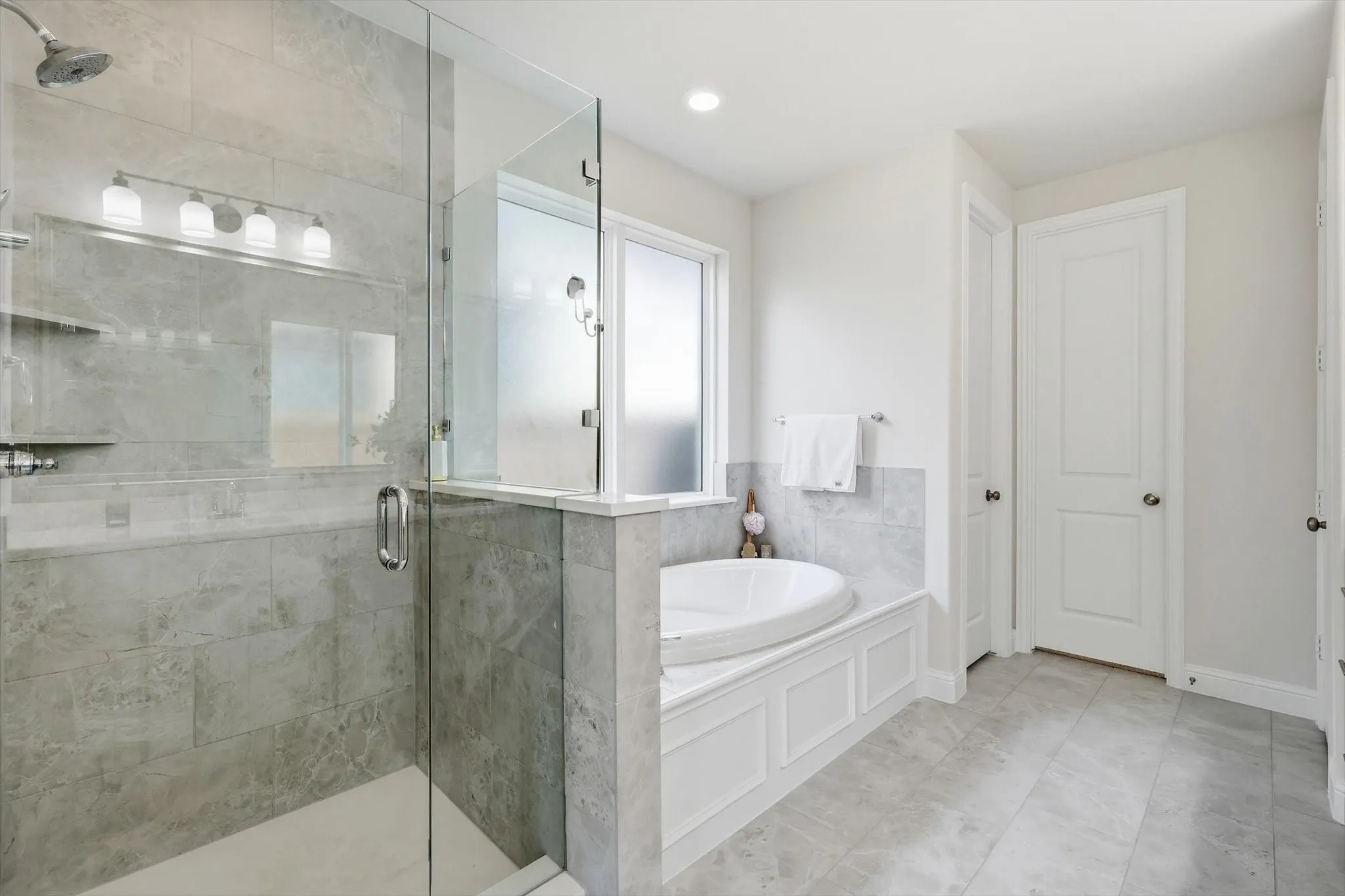 Bathroom featuring a glass-enclosed shower with a rainfall showerhead, a built-in soaking tub with paneled surround, light-toned wall and floor tiling, and white doors