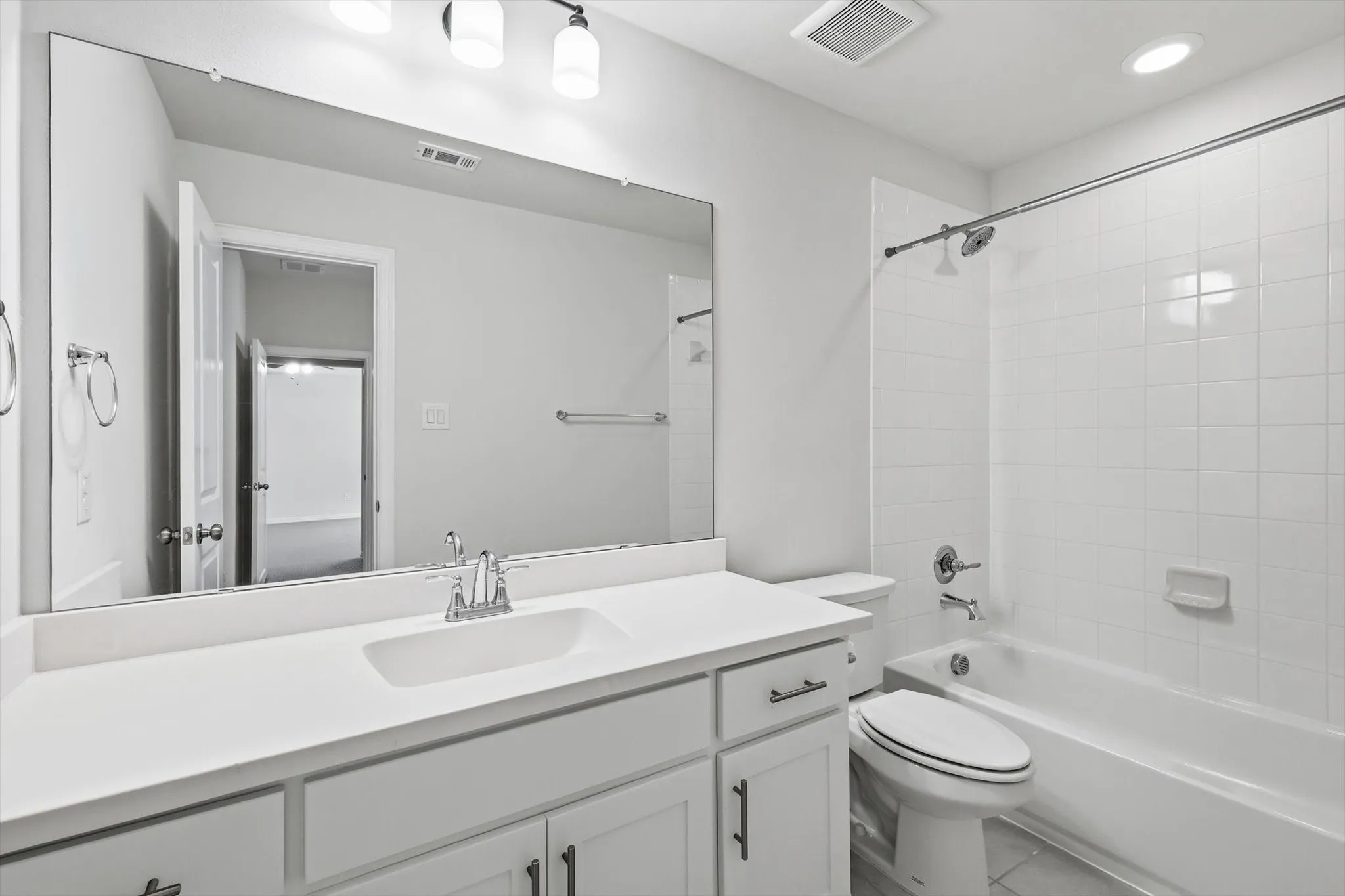 Bathroom featuring a single vanity with an integrated sink and chrome faucet, a large frameless mirror, and a built-in bathtub with a white tiled shower surround