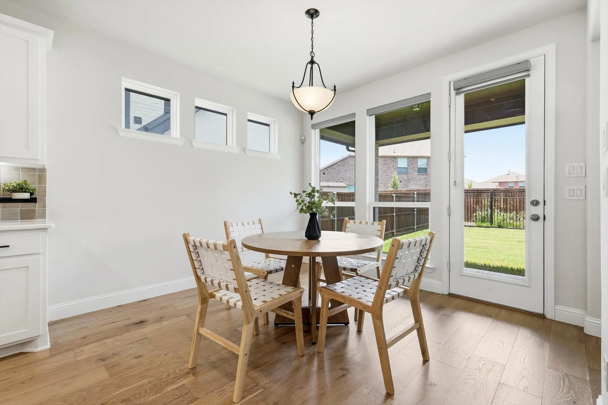 Dining area featuring wood-finish flooring, a contemporary chandelier, multiple windows, a glass-paneled exterior door, and built-in cabinetry with a tiled backsplash