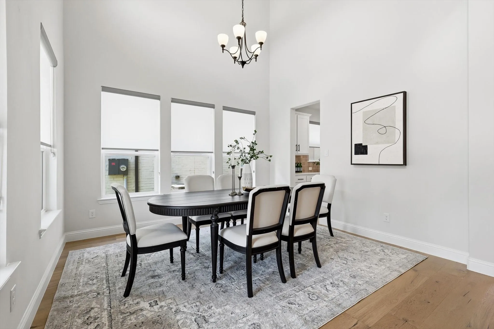 Dining space featuring high ceilings, wood-finish flooring, and multiple windows with roller shades