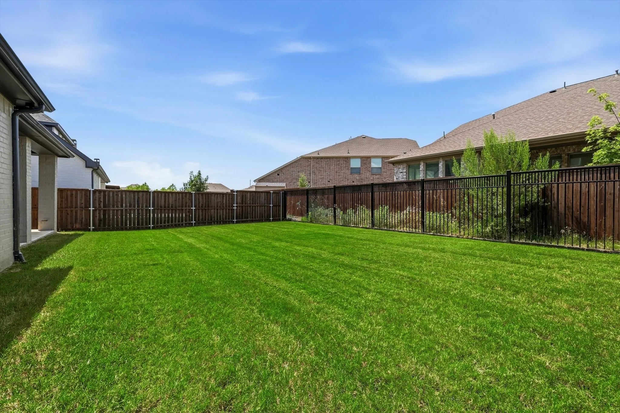 Expansive green lawn featuring a wood privacy fence and black metal fencing