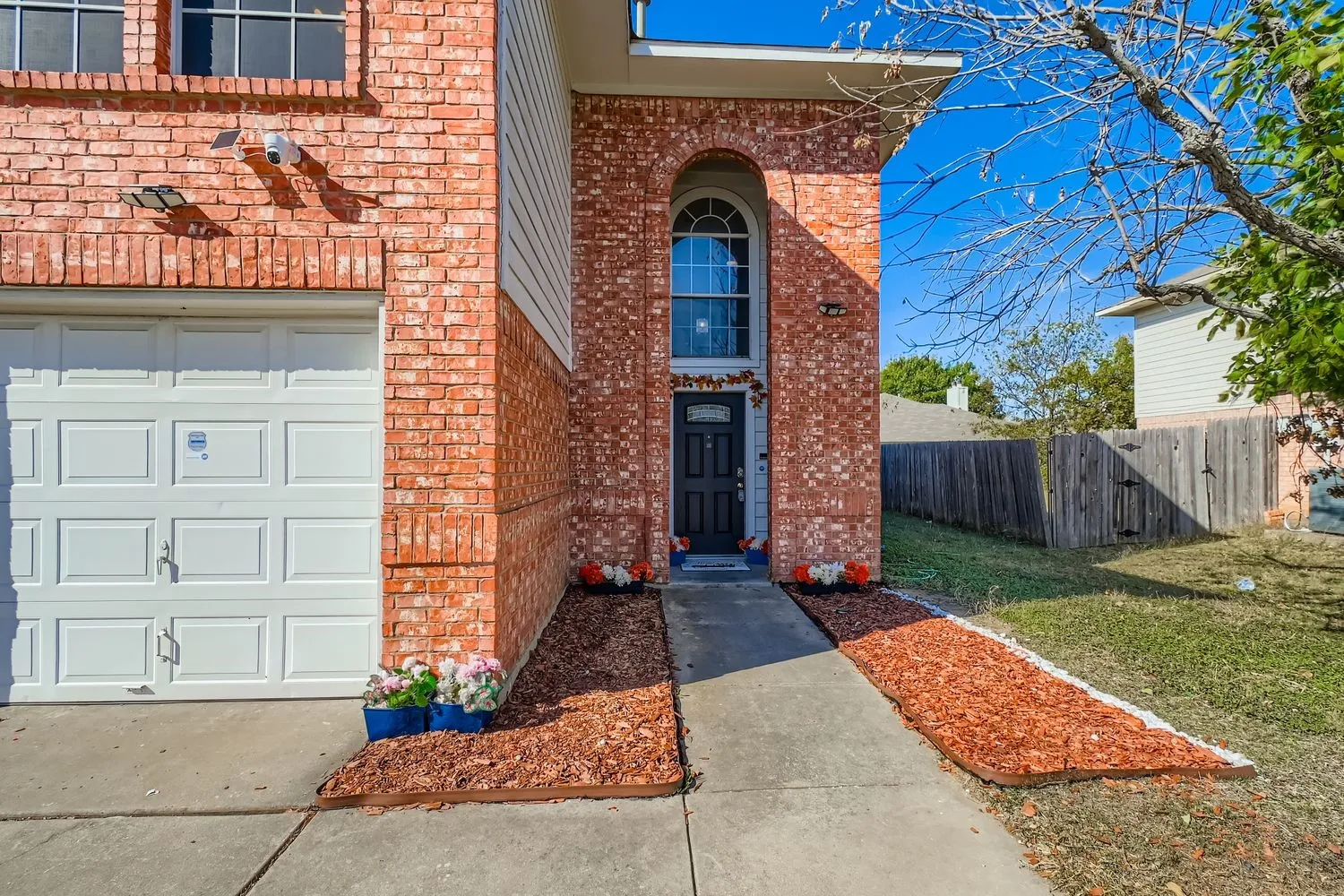 Brick facade residence featuring a prominent arched entry window, a paneled garage door, and a sidewalk leading to the front door