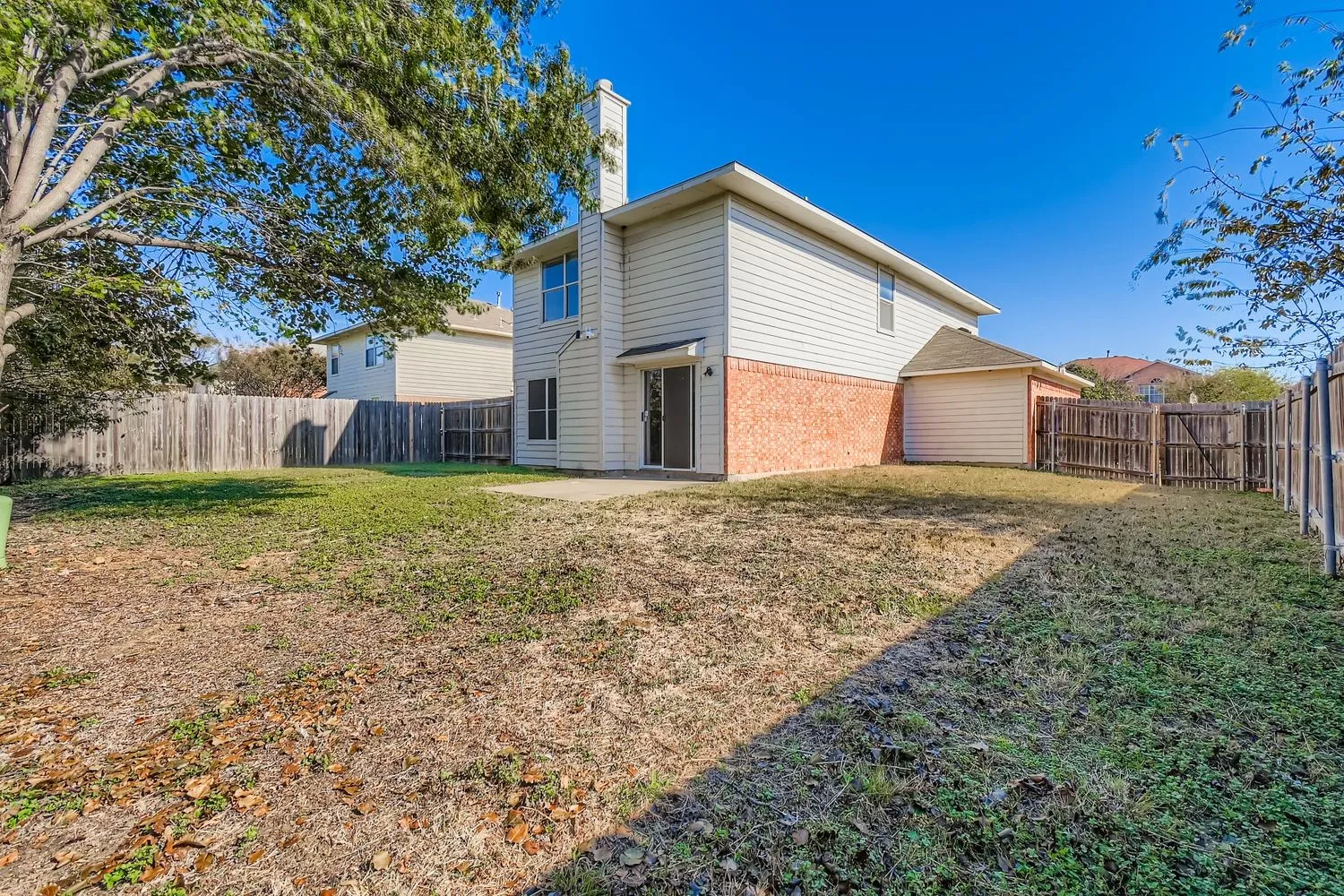 Expansive backyard featuring a privacy fence, mature trees, and a concrete patio