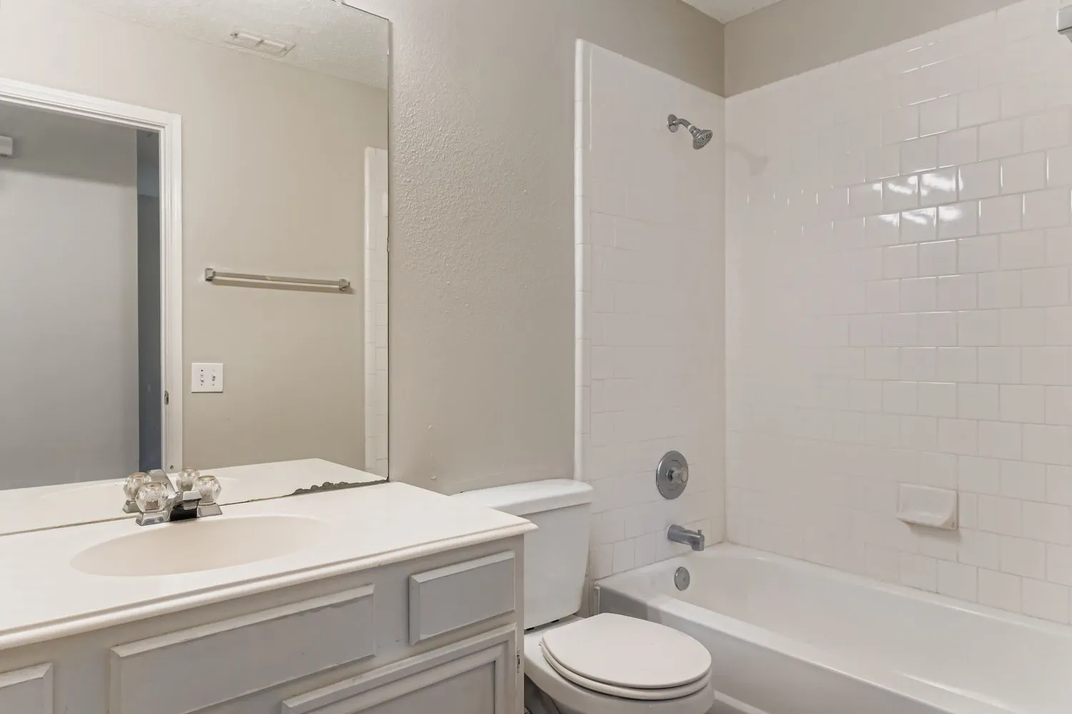 Bathroom featuring a white vanity with an integrated sink, a rectangular mirror, a toilet, and a white subway tile surround for the tub and shower combination