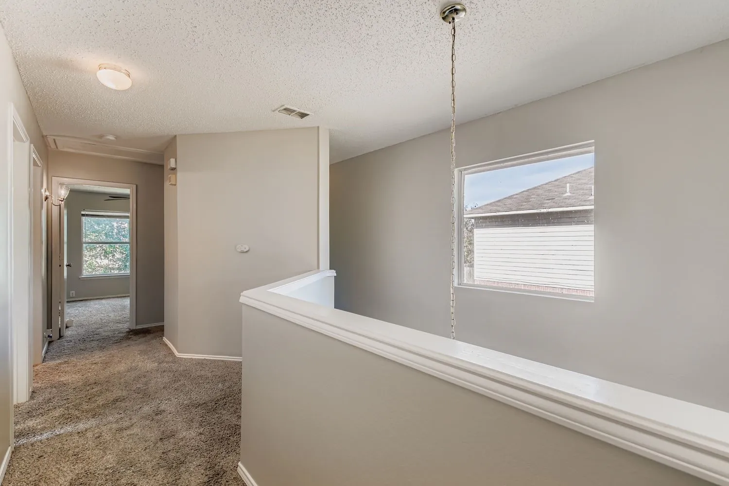 Upper-level landing featuring textured carpeting, neutral wall color, and a window with natural light