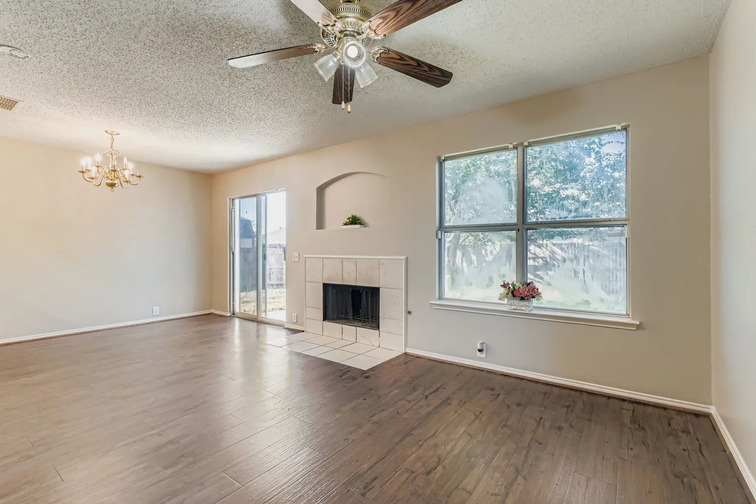 Open-concept room featuring wood-finish flooring, a tiled fireplace with an arched niche, and a ceiling fan