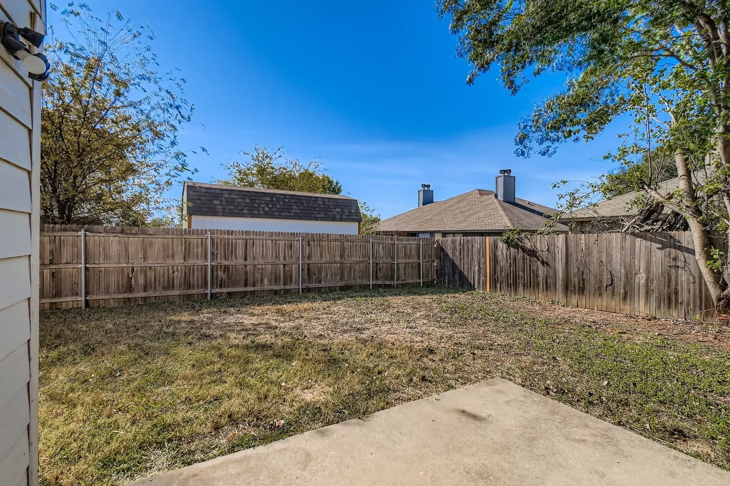 Expansive backyard featuring a concrete patio, wood privacy fencing, and a detached shed with a shingle roof