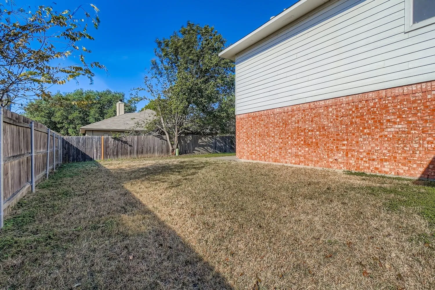 Expansive backyard area featuring a wood privacy fence, established trees, and a property exterior with brick and horizontal siding