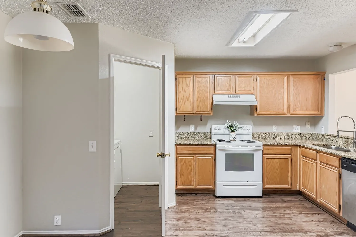 Kitchen featuring wood-finish flooring, light wood cabinetry, white appliances, and speckled countertops