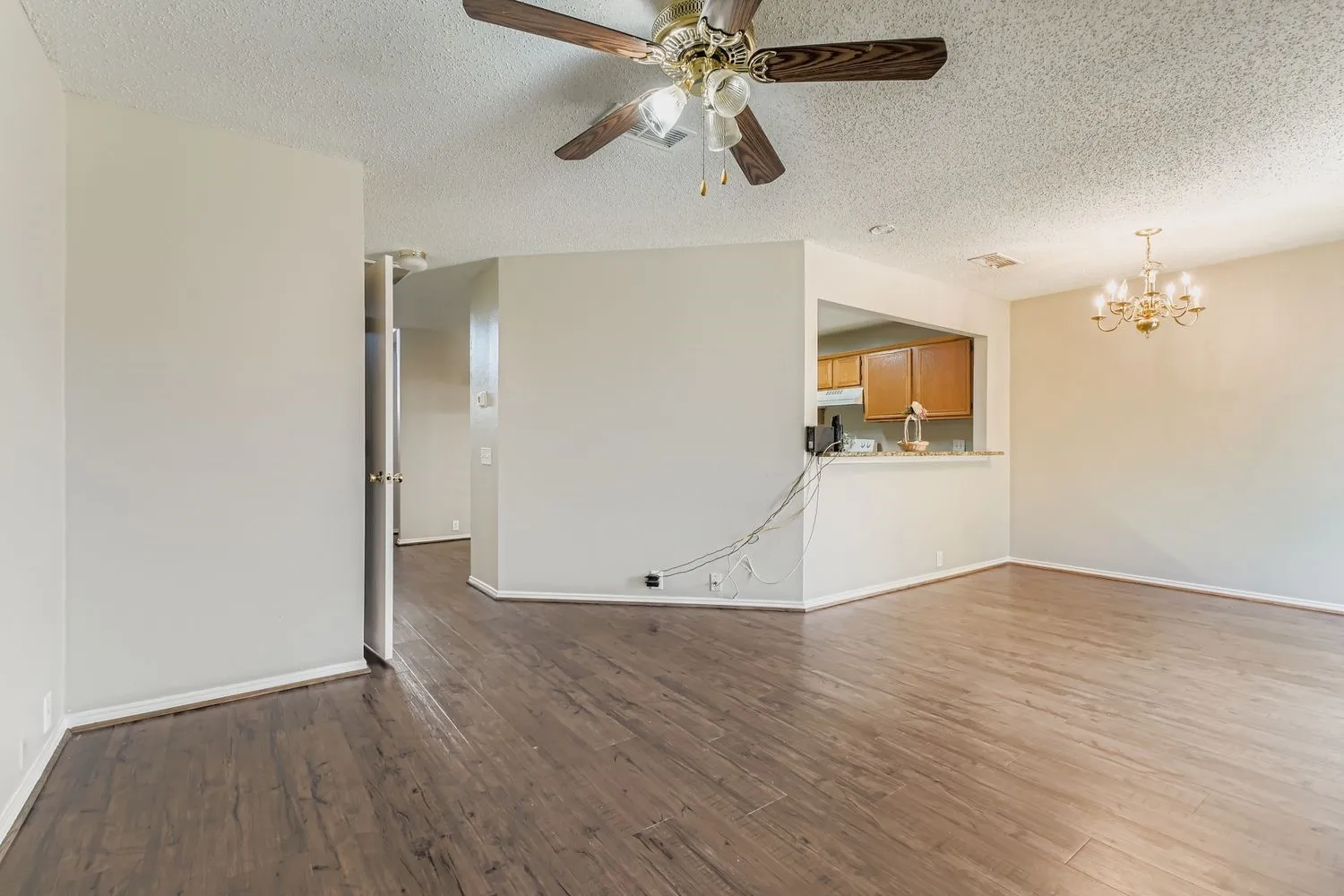 Spacious room featuring wood-finish flooring, a ceiling fan, and a gold-tone chandelier