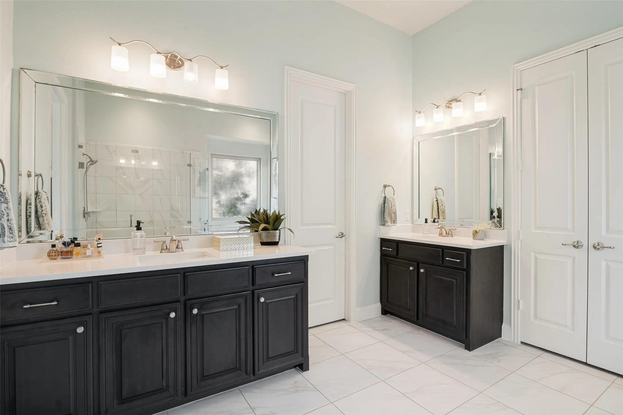 Dual vanity bathroom featuring a large framed mirror, square tile flooring, light blue wall paint, dark wood-finish cabinetry, and white countertops