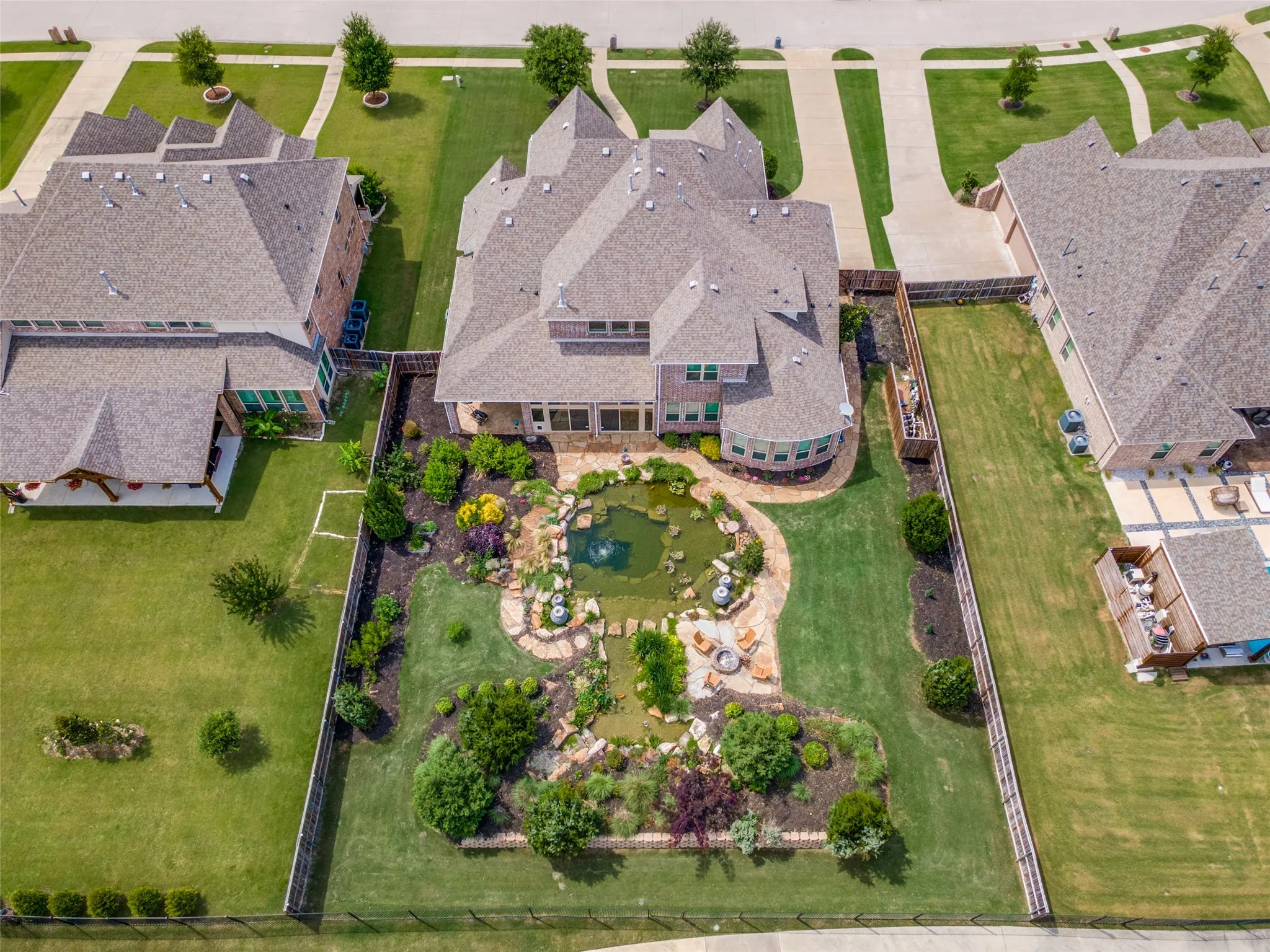 Expansive backyard featuring a natural swimming pond with water features, mature landscaping, and a manicured lawn