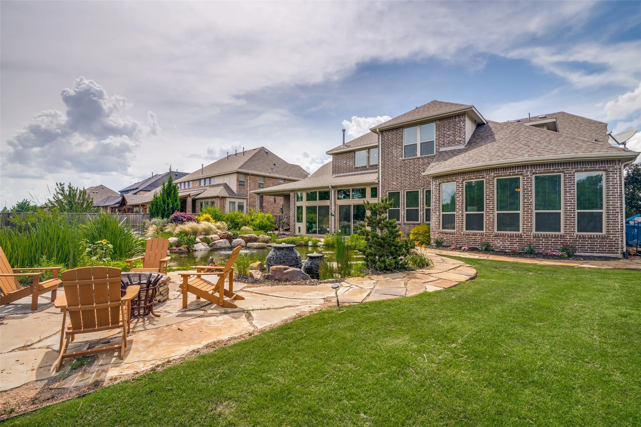 Spacious backyard featuring a flagstone patio, integrated fire pit, and a water feature surrounded by landscaping