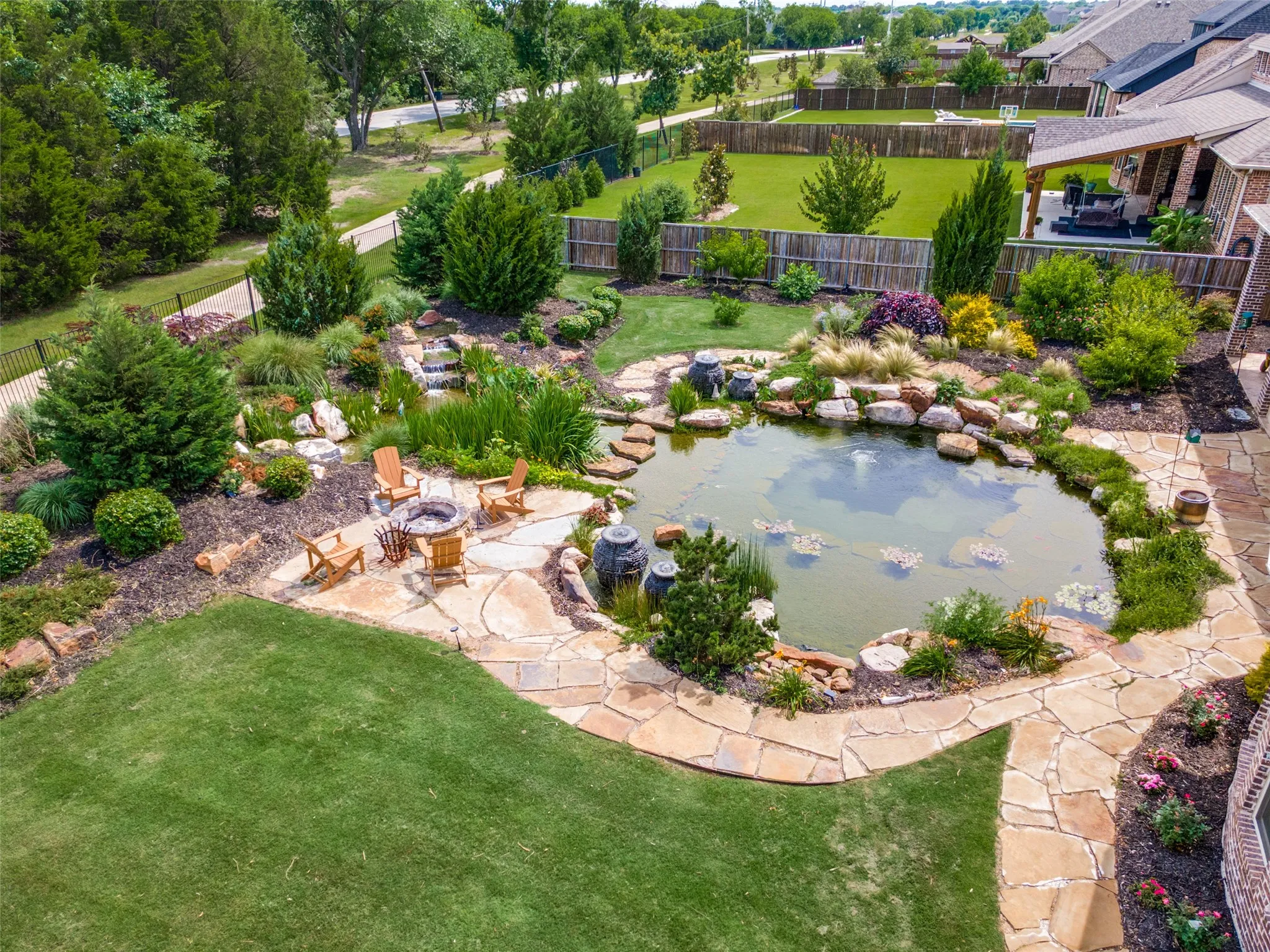 Expansive backyard featuring a natural swimming pond with water features, mature landscaping, and a manicured lawn