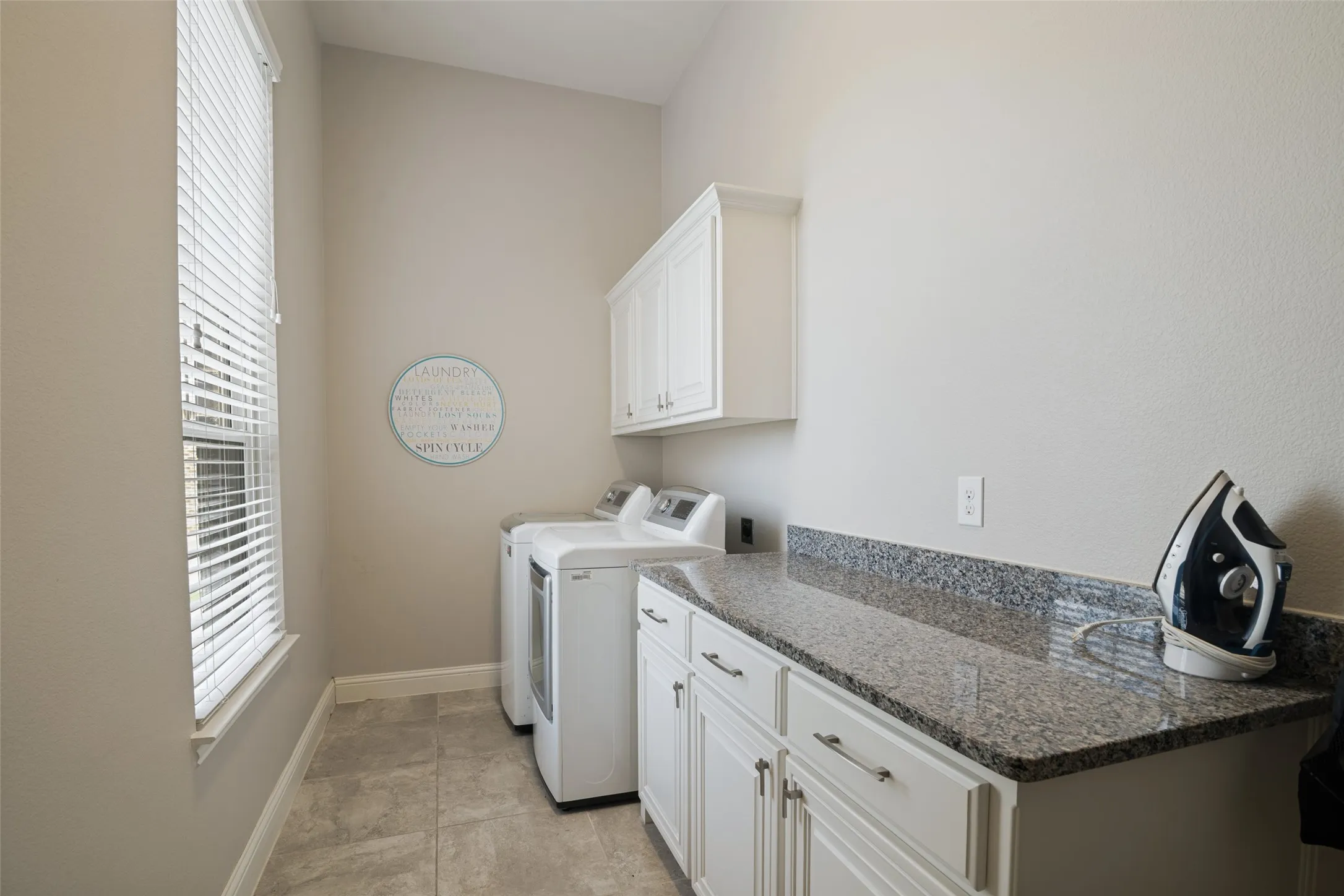 Utility room featuring granite-look countertops, white cabinetry with silver hardware, and tiled flooring