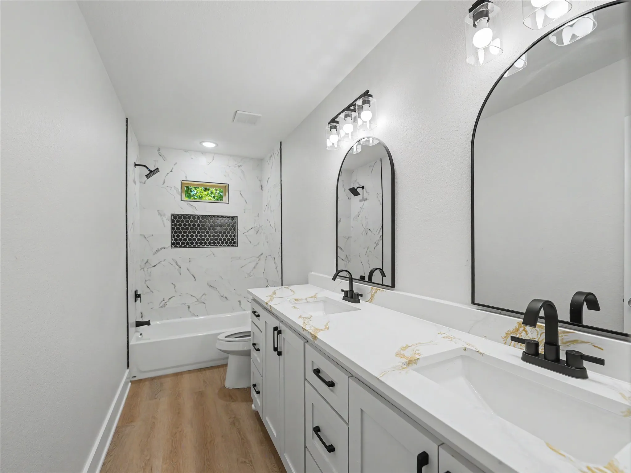Modern bathroom with a dual vanity featuring white shaker cabinetry, white countertops with gold veining, and matte black hardware