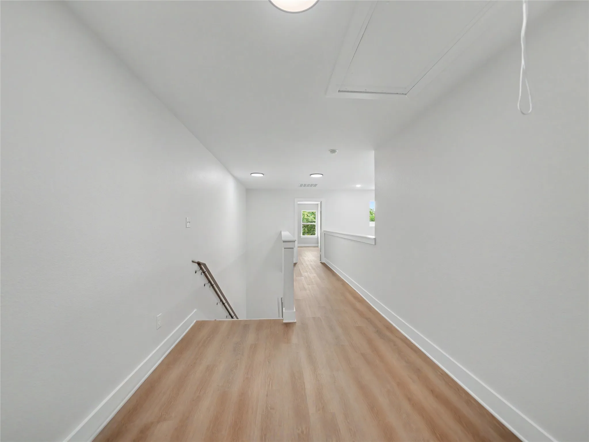 Light-toned wood-finish flooring extends through this upper-level hallway, complemented by white walls and trim
