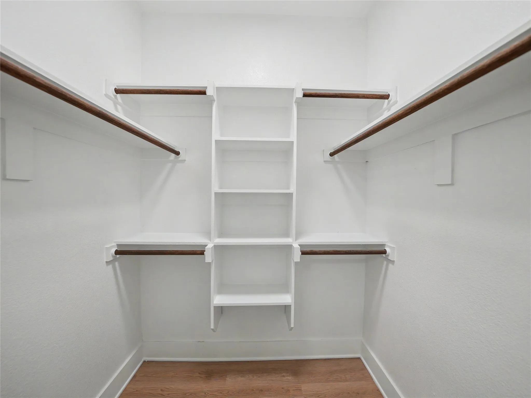 Walk-in closet featuring built-in shelving, multiple hanging rods, white walls, white trim, and wood-finish flooring
