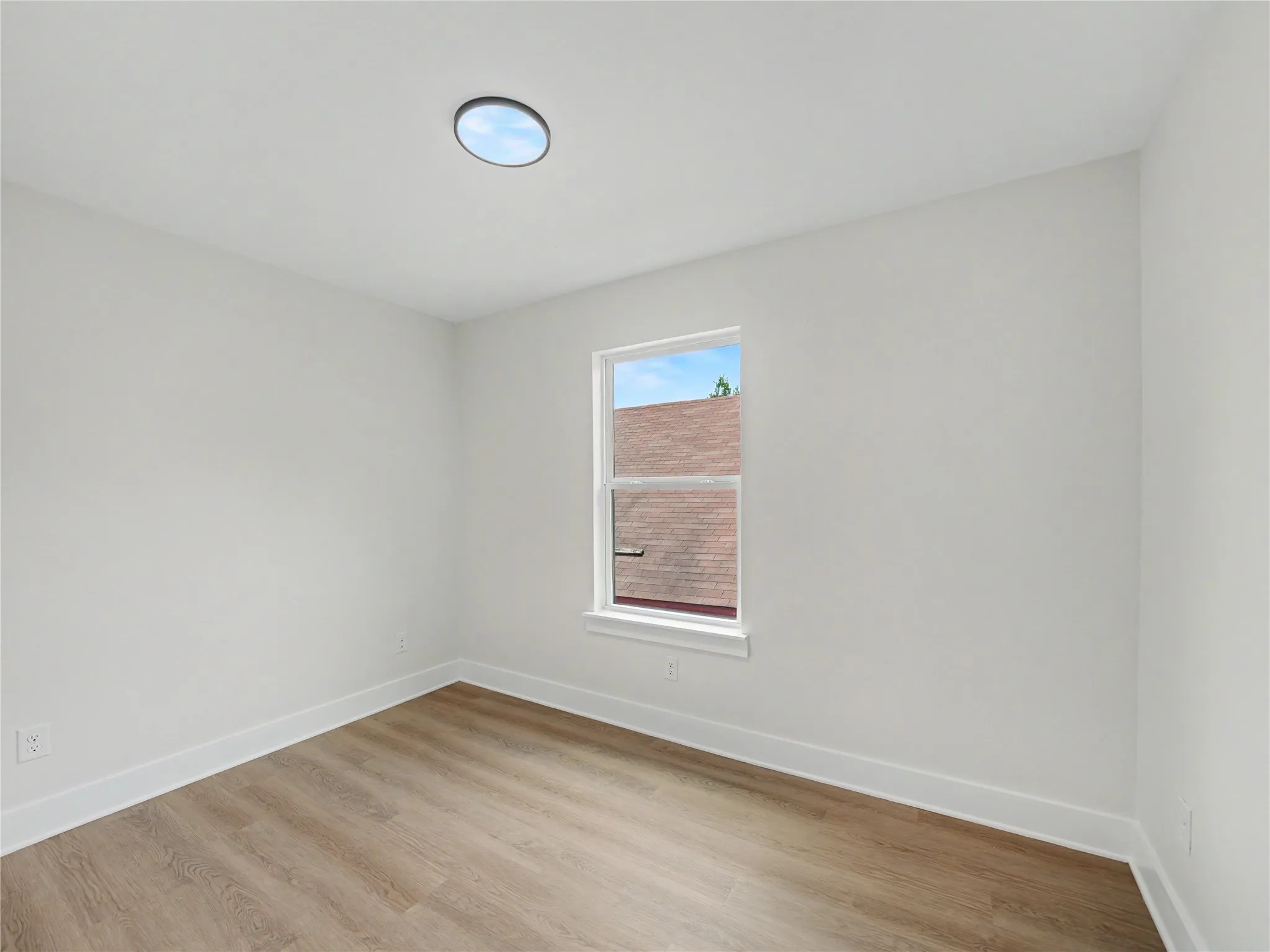 Bright interior space featuring a round ceiling light, a single window, white walls, white baseboards, and wood-finish flooring