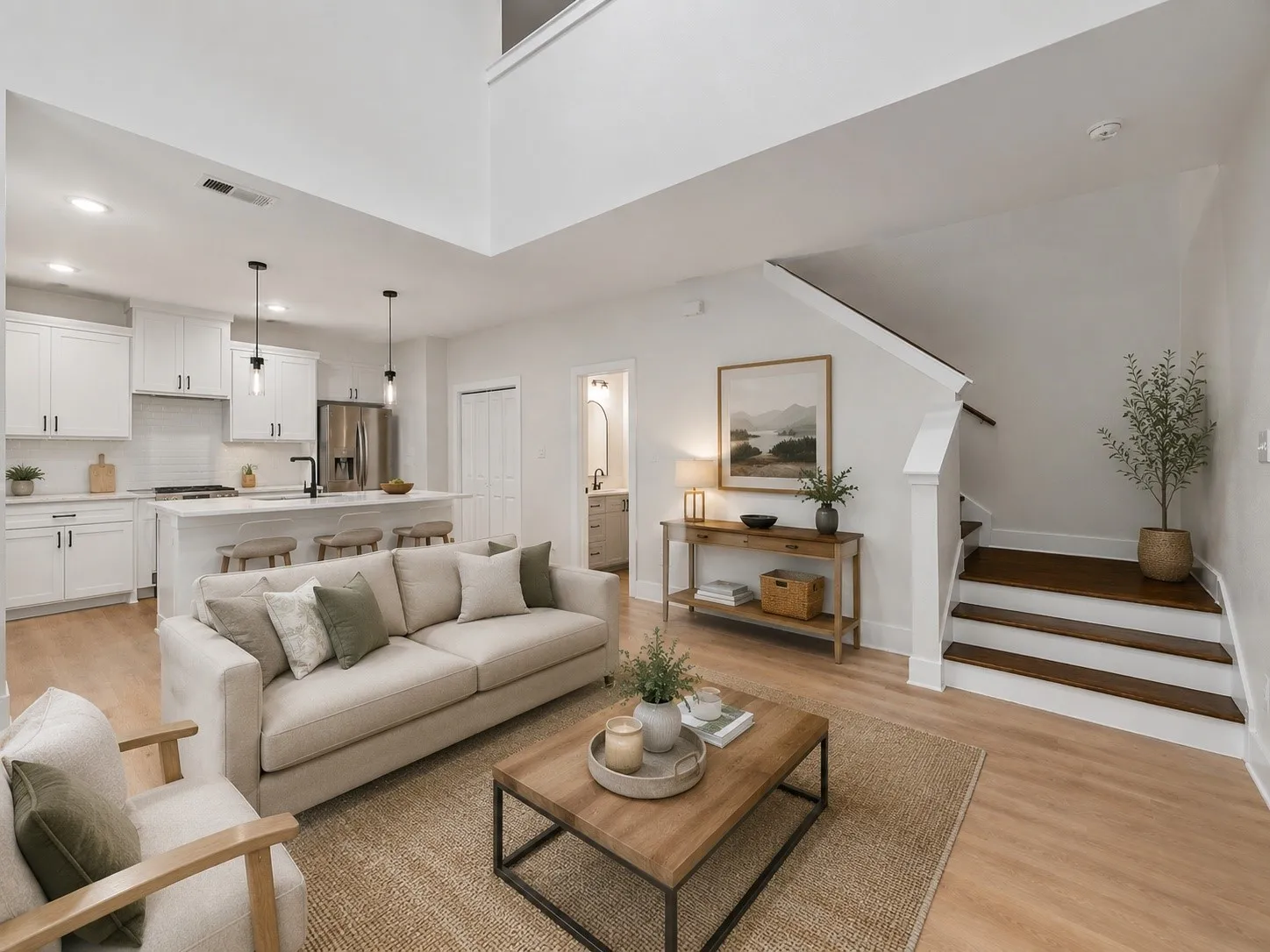 Open-concept living space featuring a two-story ceiling, light wood-finish flooring, and a contemporary kitchen with white cabinetry, a large island, and stainless steel appliances