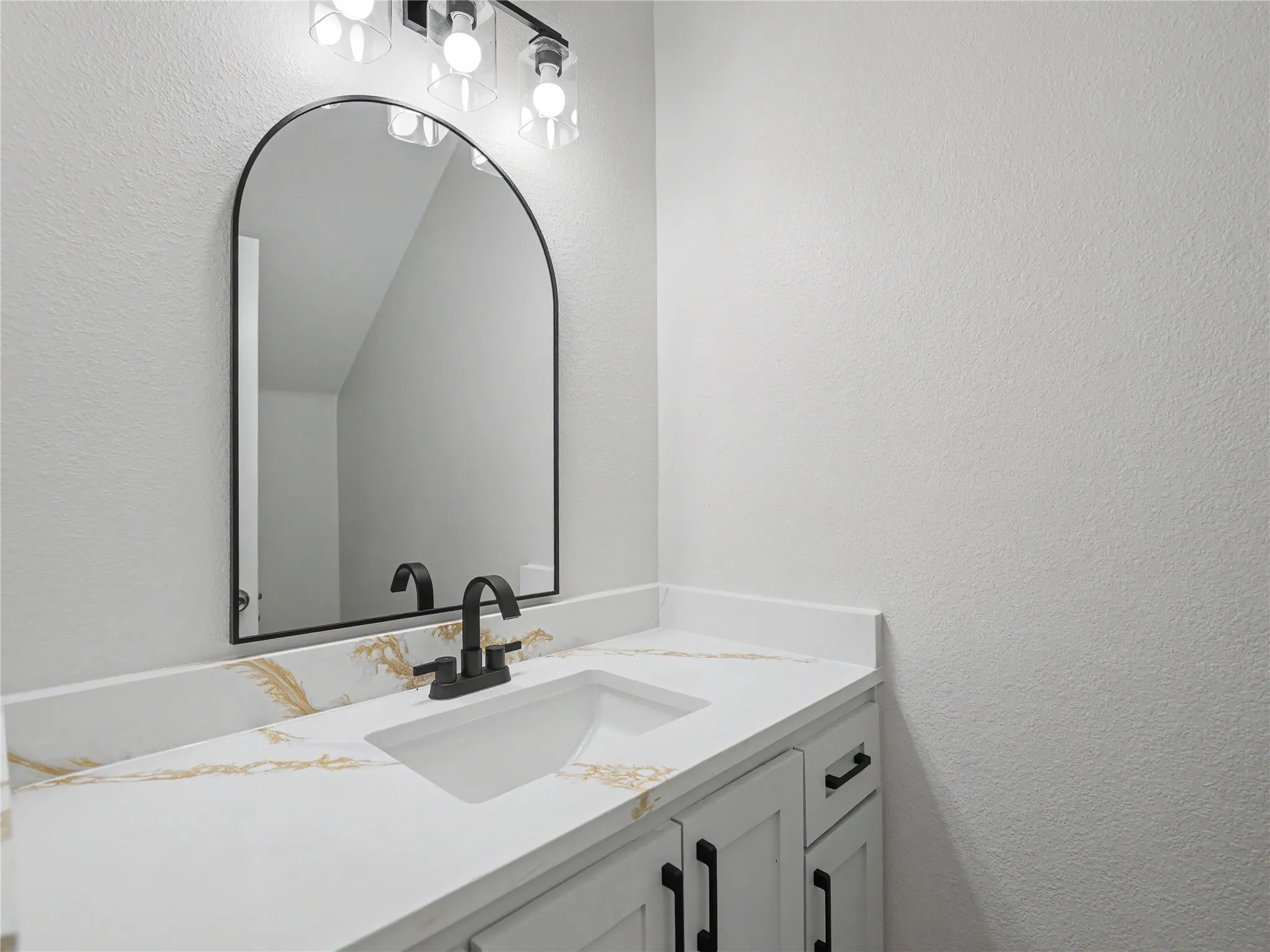 Bathroom vanity featuring a white countertop with gold veining, an undermount sink, and a matte black faucet