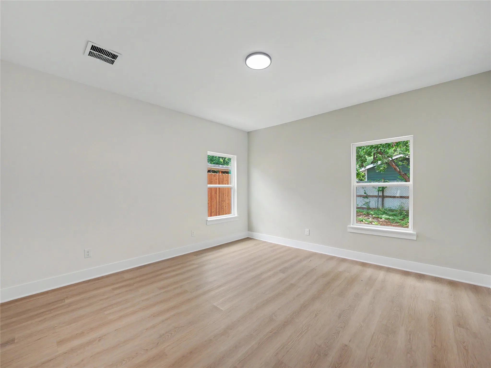 Bright room featuring light wood-finish flooring, crisp white baseboards, and two windows with white trim