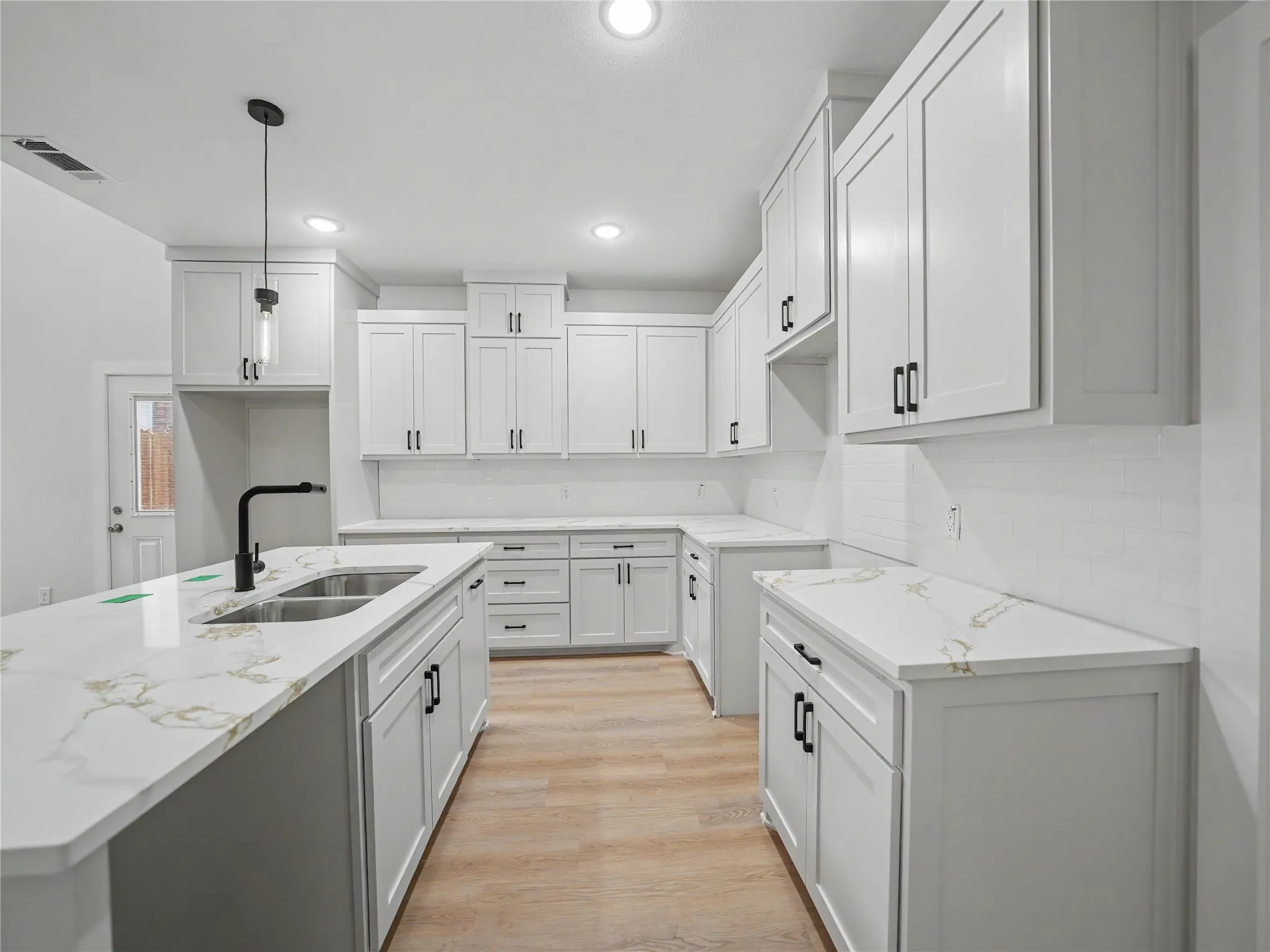 Modern kitchen featuring white shaker cabinetry with black hardware, an expansive island with a double basin sink, stone-finish countertops, and light wood-finish flooring