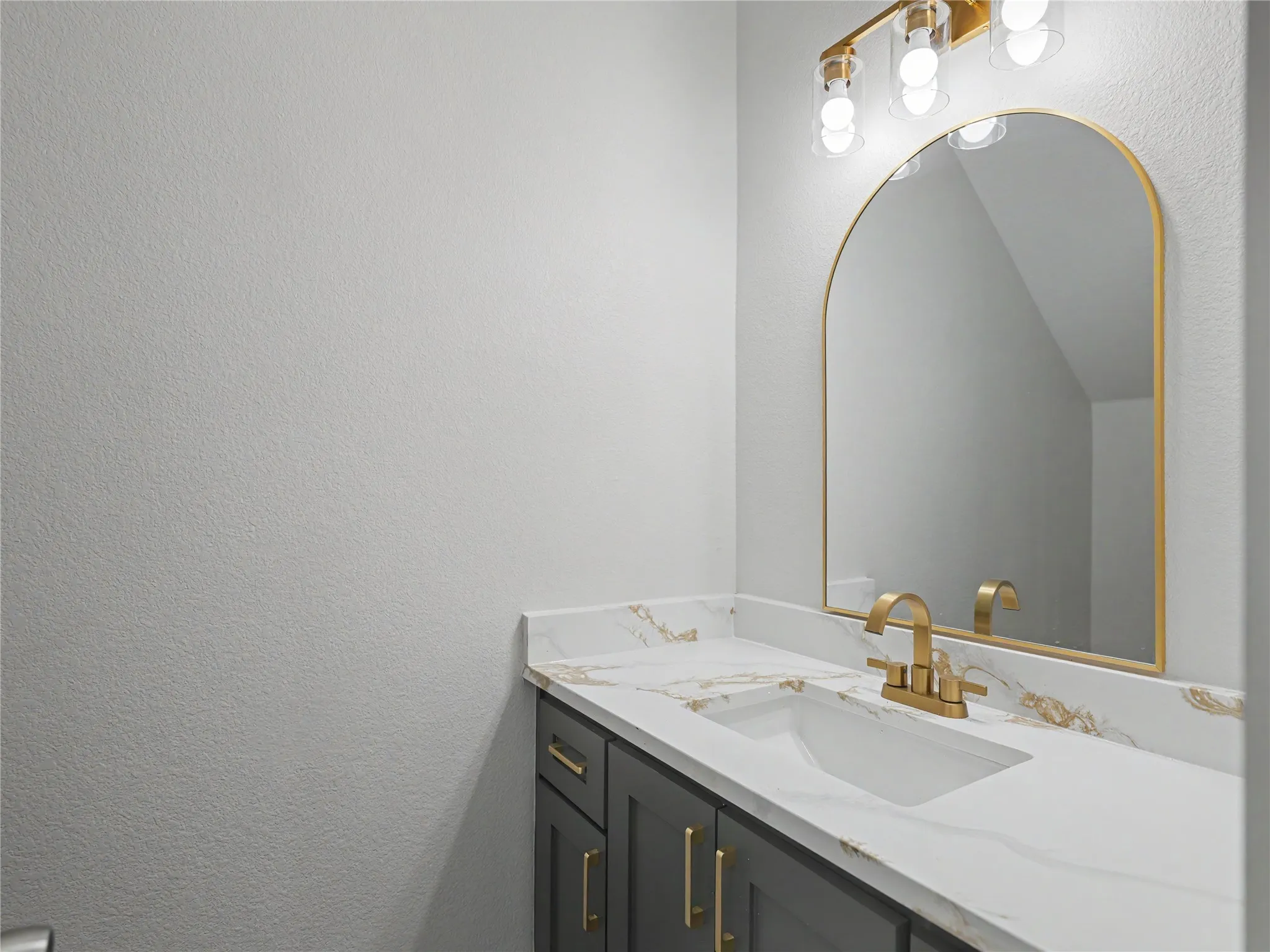 Modern vanity featuring a dark gray cabinet, quartz-finish countertop with integrated sink, and brushed gold faucet