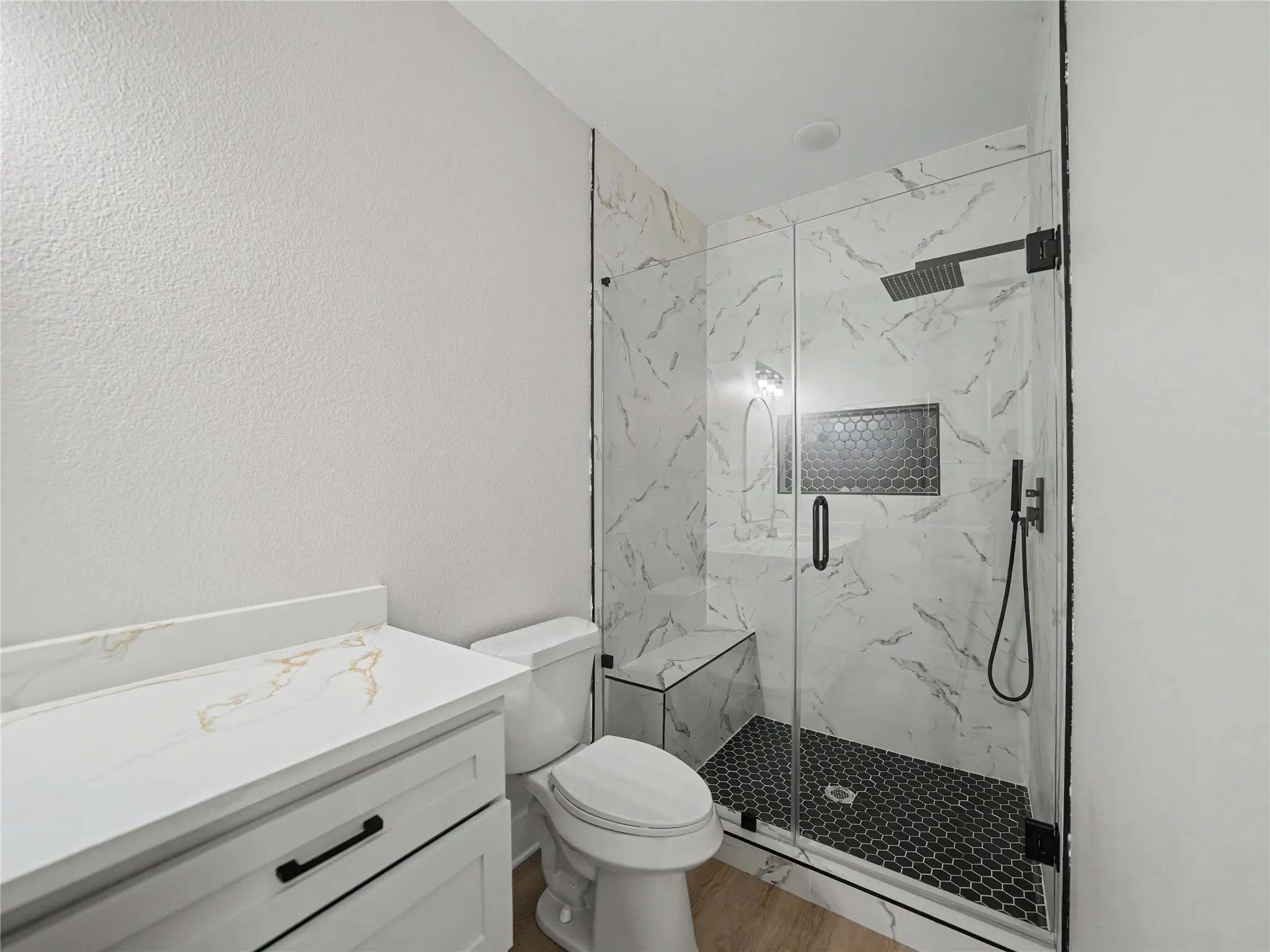 Modern bathroom featuring a glass-enclosed shower with white marble-look tile, a built-in shower bench, and a black hexagonal tile floor