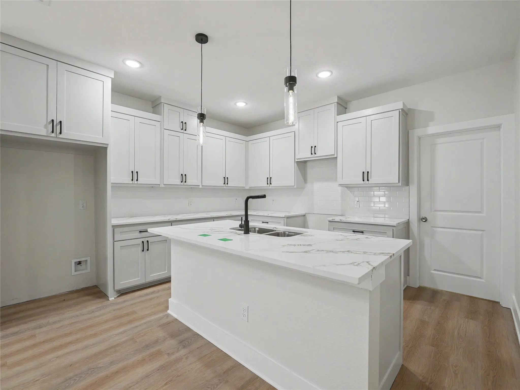 Modern kitchen featuring a central island with a waterfall-edge countertop, matte black faucet, and dual pendant lighting
