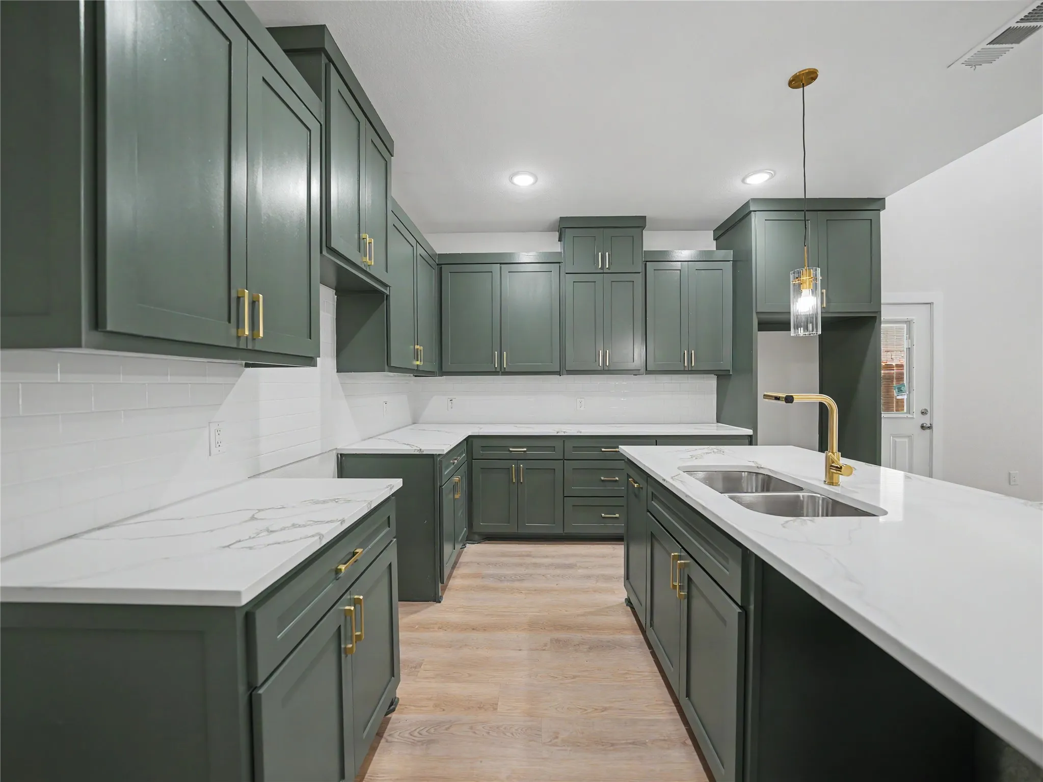 Kitchen featuring extensive green cabinetry with gold-tone hardware, white countertops, a subway tile backsplash, and wood-finish flooring