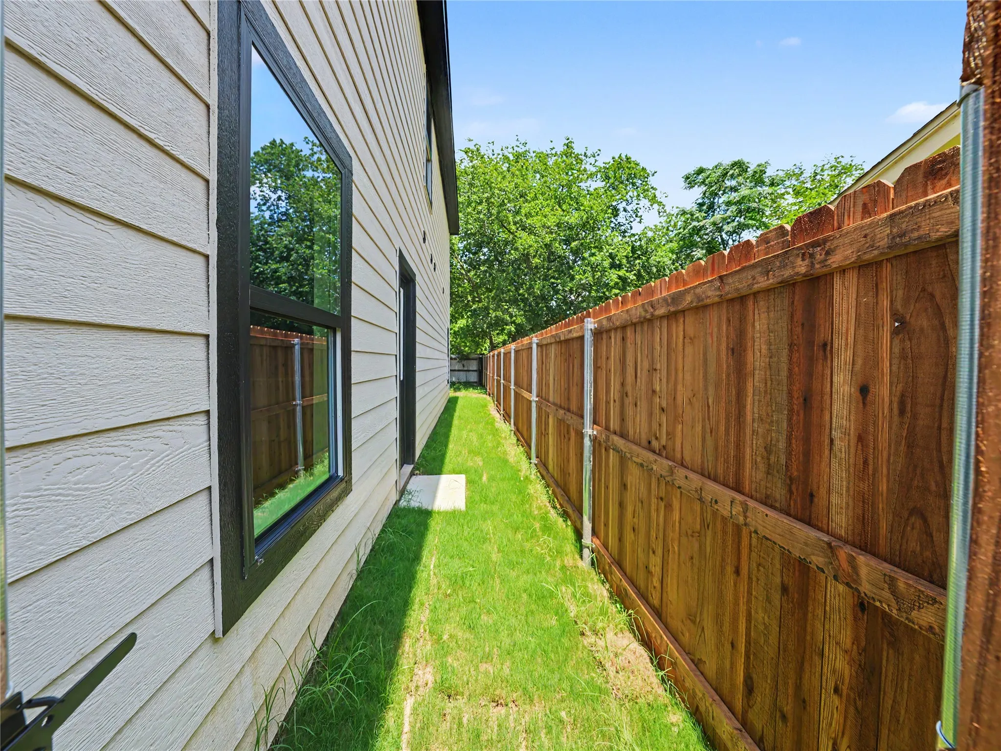 Side yard featuring a wood privacy fence, manicured lawn, and horizontal siding with dark framed windows