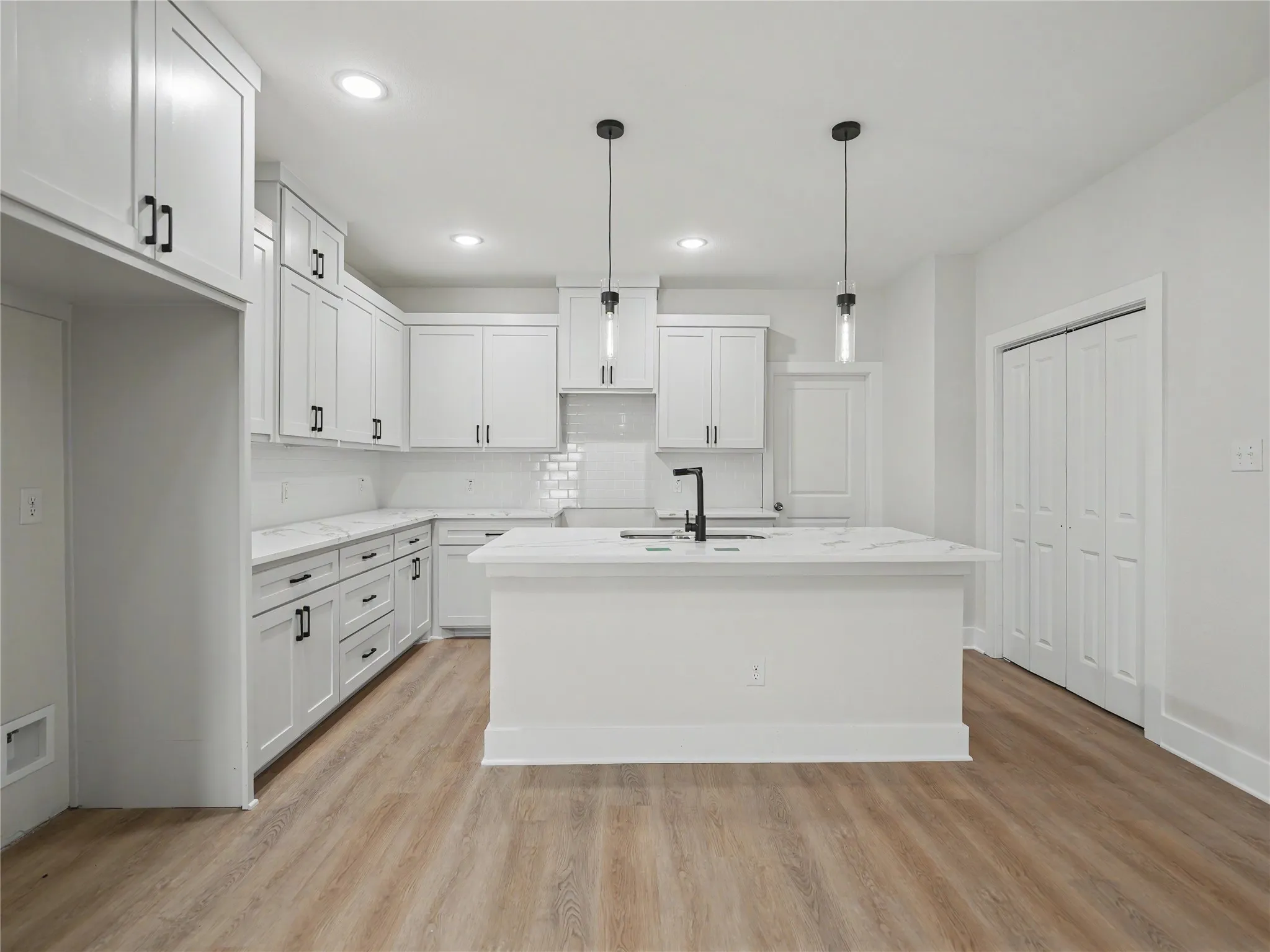 Contemporary kitchen featuring white shaker cabinetry, an island with countertop seating, wood-finish flooring, recessed lighting, and modern pendant fixtures