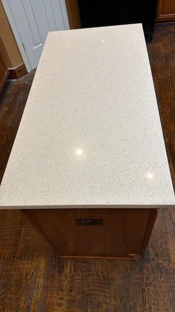 Kitchen island with a light-toned, speckled countertop and integrated power outlets, set against wood-finish flooring