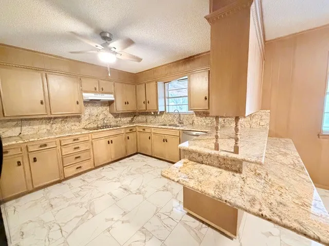 Kitchen featuring light wood-finish cabinetry, patterned stone countertops, a breakfast bar, stainless steel sink, and white tile flooring