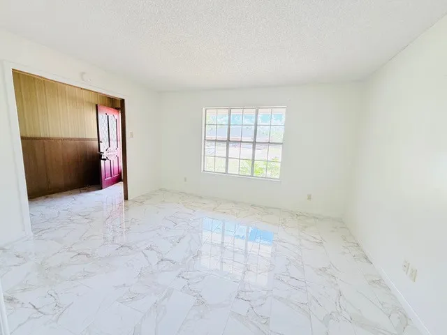 Spacious room featuring large format marble-look tile flooring, white painted walls, and a large multi-pane window