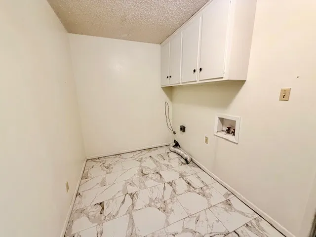 Utility room featuring patterned tile flooring, white wall-mounted cabinetry, white walls, and a textured ceiling