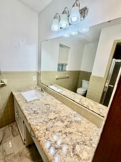 Bathroom featuring a vanity with an integrated rectangular sink, a stone-finish countertop, and a vanity light fixture with four frosted glass shades