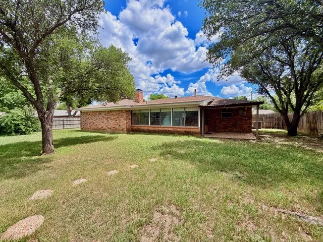 Expansive backyard featuring mature trees, a brick exterior, a covered patio, and a privacy fence