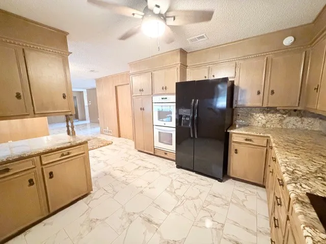 Kitchen featuring extensive wood cabinetry, granite countertops, double wall ovens, a side-by-side refrigerator, and a ceiling fan
