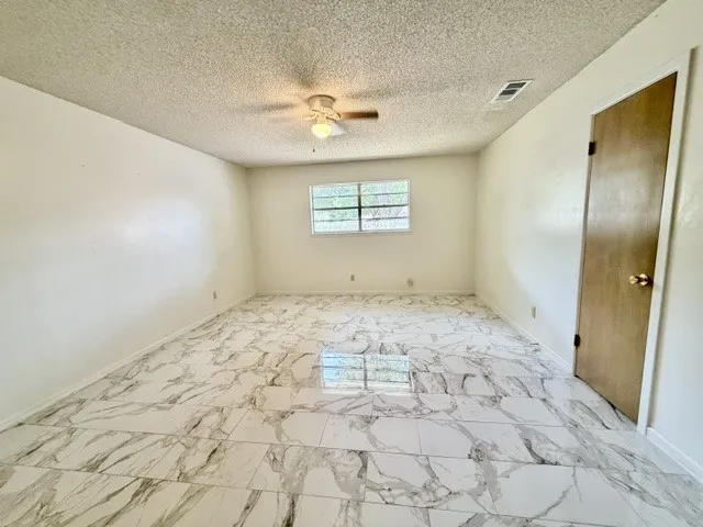 Spacious room featuring large format marble-look tile flooring and a ceiling fan