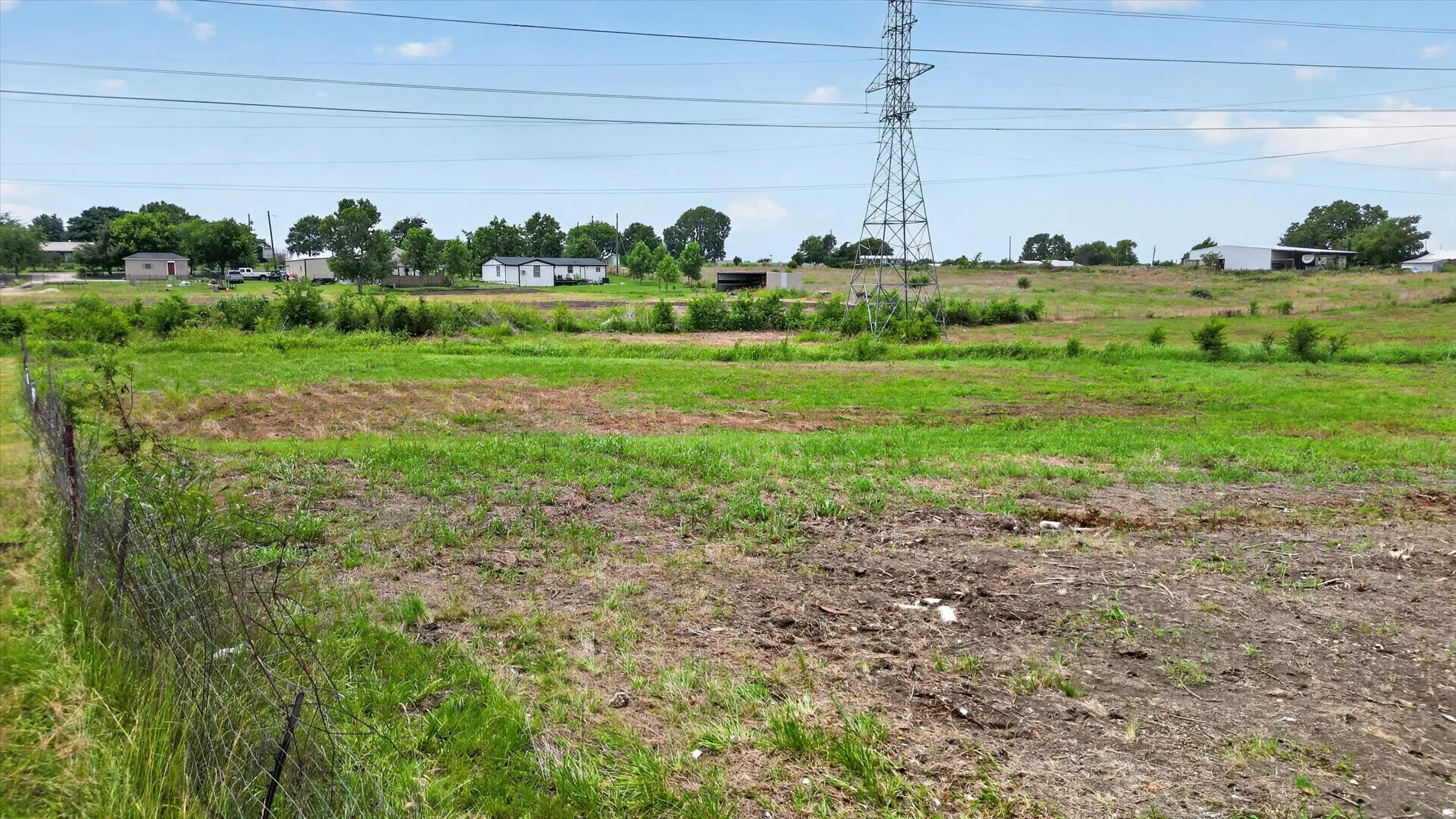 Expansive, undeveloped land parcel featuring a perimeter fence and mature trees along the horizon