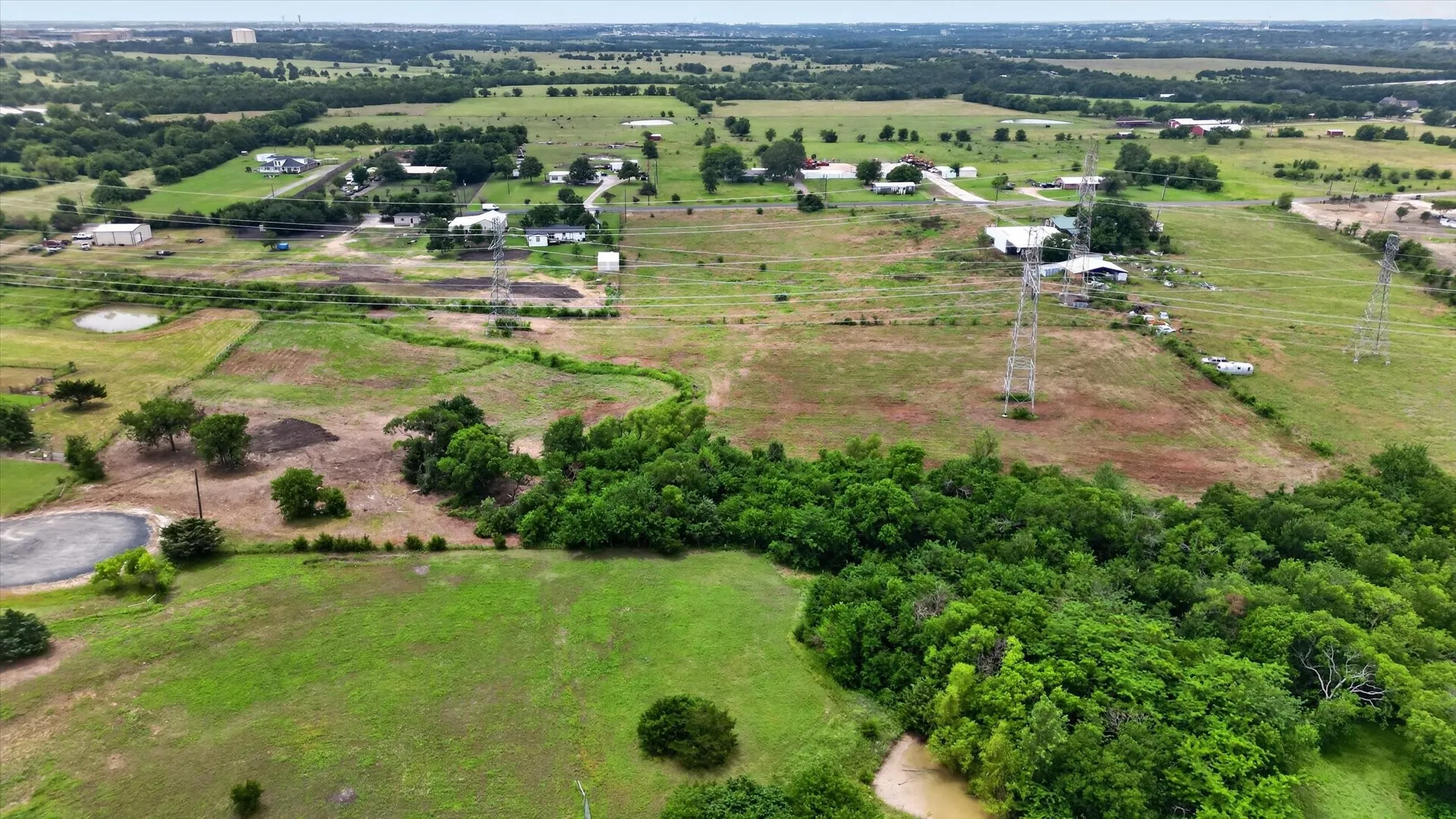 Expansive undeveloped land featuring a combination of open fields, wooded areas, and scattered residential structures