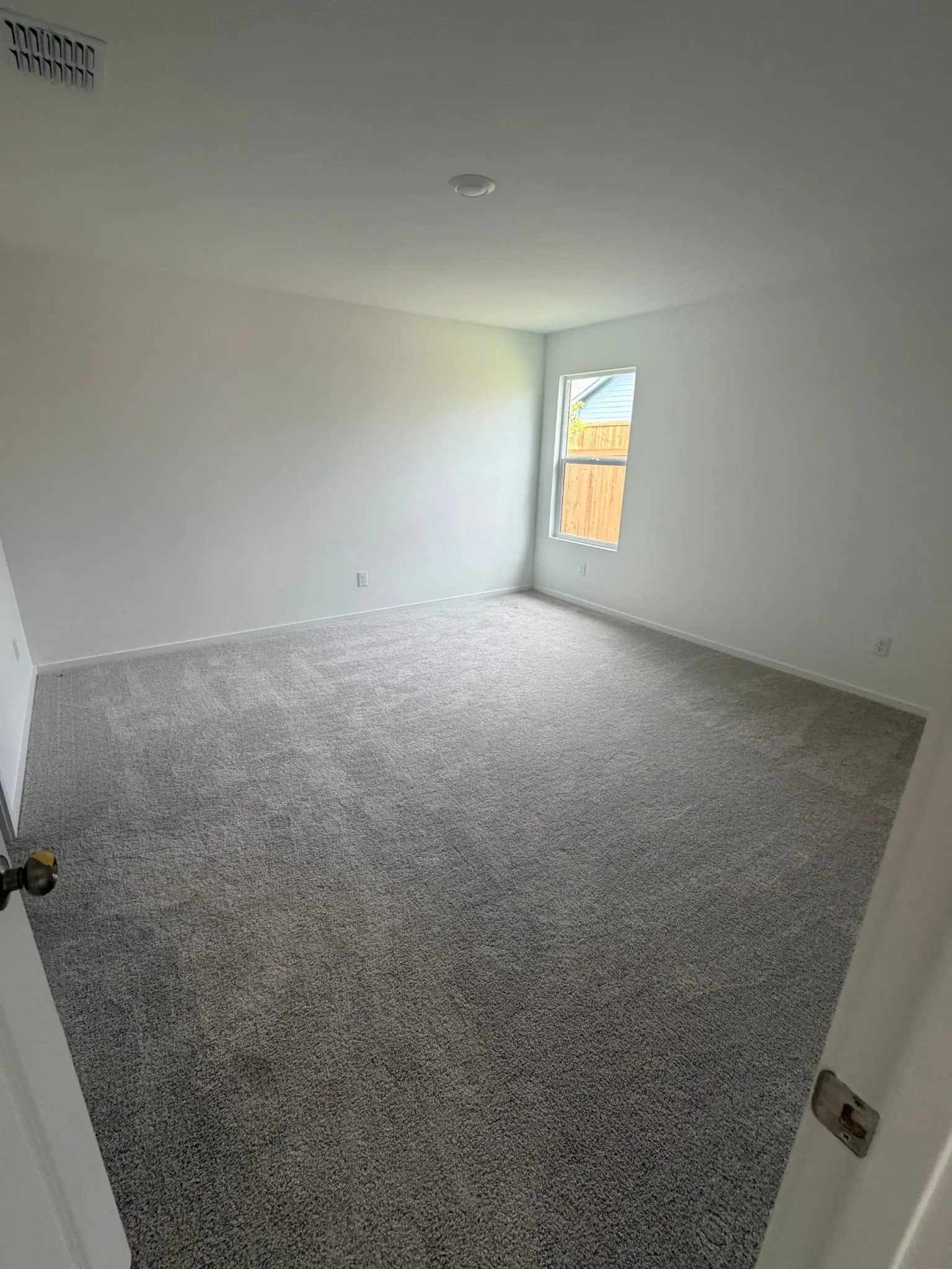 Spacious room featuring neutral carpeting, white walls, a single window, and an overhead recessed light