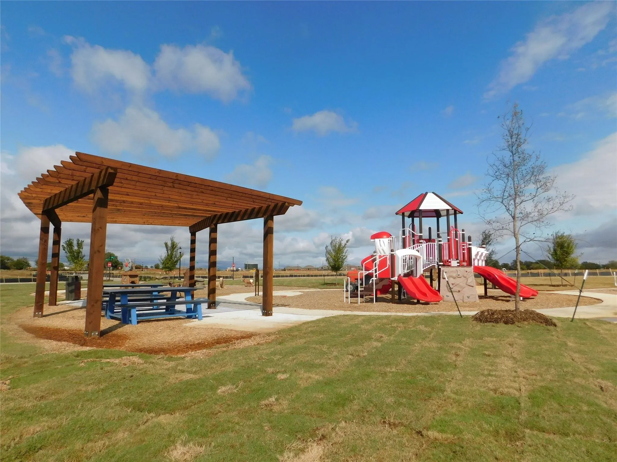 Outdoor recreation area featuring a wood pergola with a picnic table, a vibrant playground structure with multiple slides, and a manicured grassy expanse