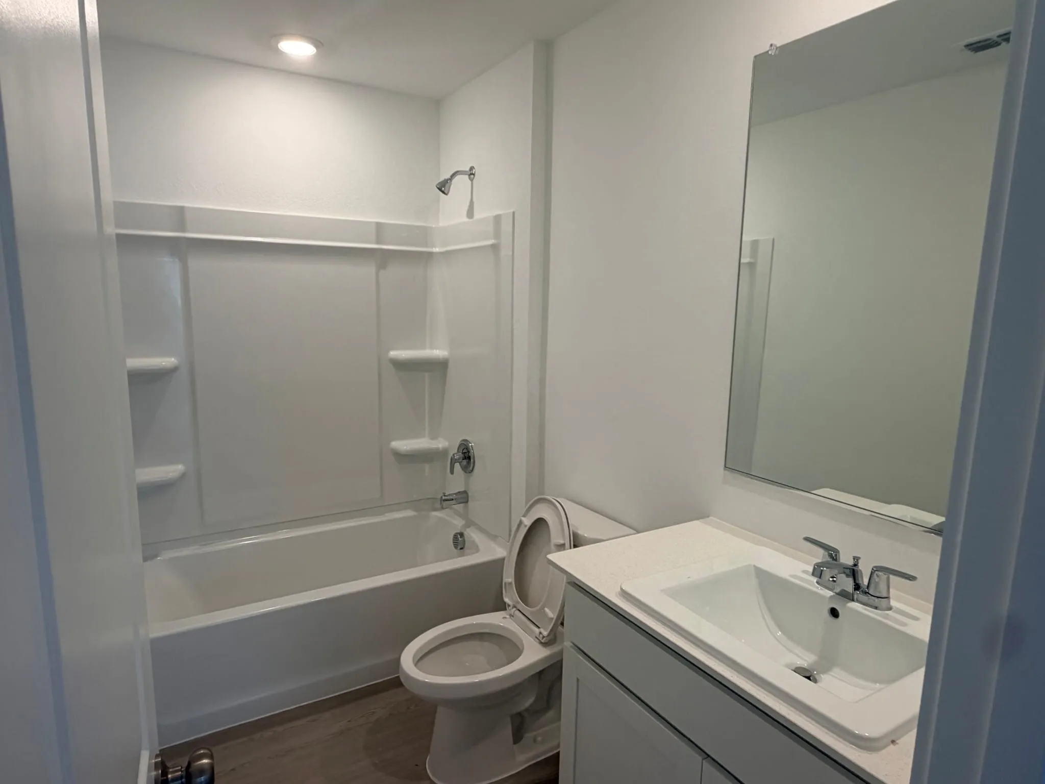 Bathroom featuring a white bathtub and shower surround, a toilet, and a vanity with an integrated sink and chrome fixtures
