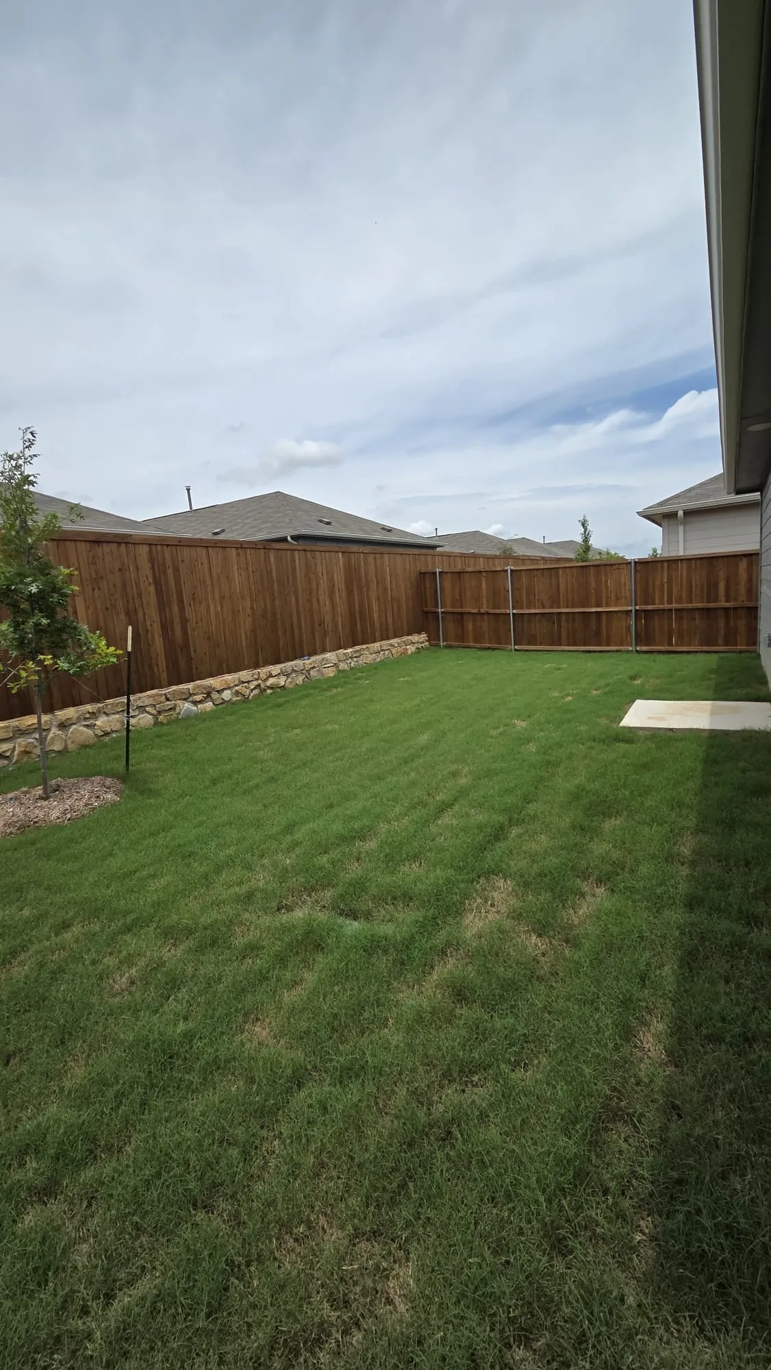 Expansive backyard featuring a lush lawn, privacy fencing, and a stone retaining wall