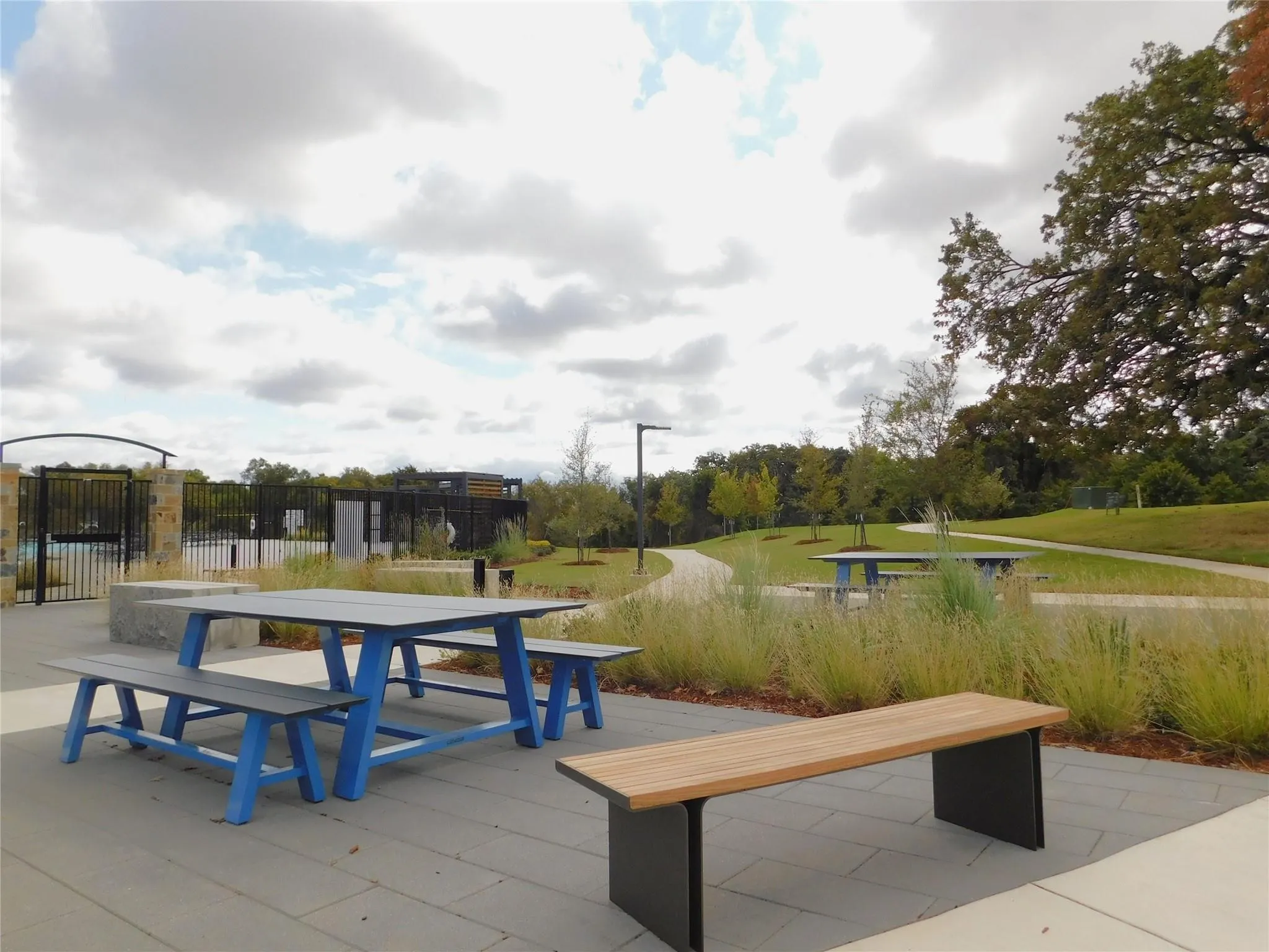 Outdoor patio space featuring modular pavers, a blue picnic table with benches, and a separate wooden bench with a dark metal base